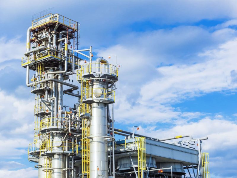 Two absorption columns stand at the gas processing plant against the blue sky.